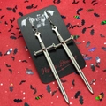 Close-up of silver gothic sword earrings on a bat-patterned card with red background - Sword