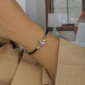 Detail of woven bracelet with gold and silver heart wing pendant on a wrist - Two-Tone Cord Bracelet
