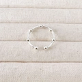 Detailed view of silver bow-shaped ring with small beads on a beige linen background - Bead Style