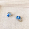 Close-up of hoop earrings with clear blue pendants containing dried floral elements - Silver + Blue
