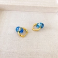 Detail of gold earrings with blue dried flower resin charms on white textured fabric - Gold + Blue