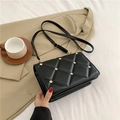 Black quilted crossbody bag with gold studs on a white fabric with casual blazer - Black