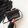 Elegant black woven cylinder bag with gold clasp and textured glossy finish - Black