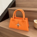 Chic bright orange leather tote bag featuring a silver star metal clasp on wooden steps - Orange