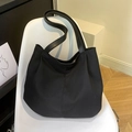 Borsa tote minimalista in tela nera con manici in pelle e logo esposta su sedia bianca - Nero