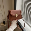 Classic brown messenger bag with gold metal clasp held by hand in soft window light - Brown