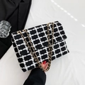Bolso bandolera de tweed blanco y negro con cadena dorada sujeto en la mano - Negro