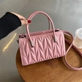 Pink quilted shoulder bag with wavy texture and silver accents on a wooden stool - Pink