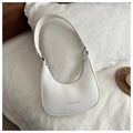 Detalle de bolso de hombro blanco de media luna con logo FASHION en una cama - Blanco
