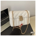 Detail of white quilted crossbody bag with golden turn-lock and chain strap on a desk - White