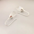 Minimalist silver hooks earrings with transparent capsule stones on a grey surface - White