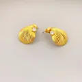Muschelförmige Goldohrringe mit Diamantakzent auf hellem minimalistischem Hintergrund - Gold