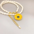 Detailed macro view of yellow enamel sunflower pendant on a white baroque pearl necklace - Yellow