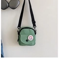 Detail of light green canvas crossbody bag featuring adjustable black strap and cute badge - Green