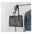 Dark grey canvas tote bag with black handles and metal studs hanging on a rack - Gray