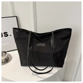 Detalle de un bolso tote grande de nailon negro con un parche sobre una mesa blanca - Negro