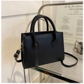 Detalle de bolso negro minimalista con herrajes dorados en estante metálico - Negro