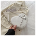 White heart-shaped PU leather crossbody bag with metal rivets and strap on casual background - White