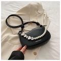 Detail of black saddle bag with heart metal and pearl chain on cream blazer background - Black