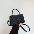 Detail of black faux leather handbag featuring a round gold buckle and a curved top handle - Black
