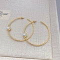 Pendientes de aro dorados con perlas blancas sobre fondo beige, vista de producto a 45 grados - Dorado