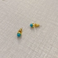 Minimalistische goldene Ohrstecker mit blauen Achatsteinen auf grauem Stoffhintergrund - Türkis-Textur-Stil / Türkisblau