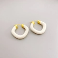 Modern gold-plated earrings with cream enamel finish on a neutral gray background - Beige