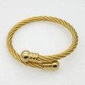 Detail of twisted cable gold bracelet with spherical end caps on a textured surface - Gold