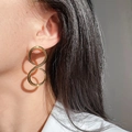 Detail von übergroßen goldenen Ohrsteckern in 8-Form mit glänzendem Metallic-Finish - Gold