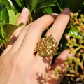 Anello a fascia larga con fiori dorati e petali testurizzati indossato sulla mano - Oro