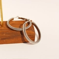 Orecchini a cerchio con spirale d'argento esposti su un blocco di legno marrone scuro - Oro bianco