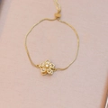 Detailed view of rotating five-petal flower charm with inlaid zircons on gold bracelet - White