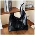 Detail of minimalist black PU leather tote bag with adjustable strap on a bookshelf - Black