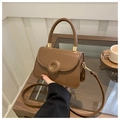 Detail of brown leather handbag featuring gold circular metal buckle and a thick handle - Brown