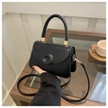 Close-up of black square handbag with golden hardware and leather strap in hand - Black