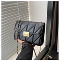 Detalle de bolso acolchado negro con cierre giratorio dorado y correa de cadena elegante - Negro
