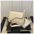 Detailed shot of cream crossbody bag with scalloped flap and gold chain on black chair - Off White
