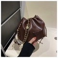 Détail d'un sac seau marron brillant avec chaîne dorée et écusson logo de mode - café