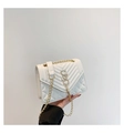 Macro shot of white quilted flap bag featuring gold S-logo and metal tassel detail - White