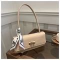 Dettaglio borsa beige con chiusura dorata e foulard in seta motivo H su un tavolino - Cachi