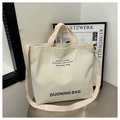 Detailed view of cream canvas tote bag with black typography on a sleek metal table - White
