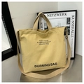Detailed view of yellow canvas tote bag with adjustable shoulder strap on metal surface - Khaki