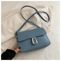 Detailed close-up of a dusty blue crossbody bag with a silver trapezoidal lock on a blazer - Blue
