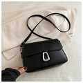 Detail of a black leather crossbody flap bag with silver U-shaped metal buckle on a white coat - Black