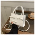 Dettaglio borsa bianca con fiocchi 3D e perle metalliche su un tavolo di legno massello - Bianco