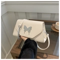 Close-up of a cream crossbody bag with a large silver butterfly clasp and chain detail - White