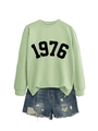 Close-up of light green 1976 printed sweatshirt with distressed denim shorts detail - Olive Green Sweatshirt (Black Font)