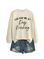 Detail of white crewneck sweatshirt with You Had Me At Day Drinking print and denim shorts - Sand (Black Print)