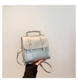 Detail eines silbernen PU-Lederrucksacks mit goldenen Metallschnallen und Klappendesign - Silber