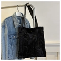 Detalle de bolso tote negro con textura de hojas, asas de cuero y cierre dorado - Negro